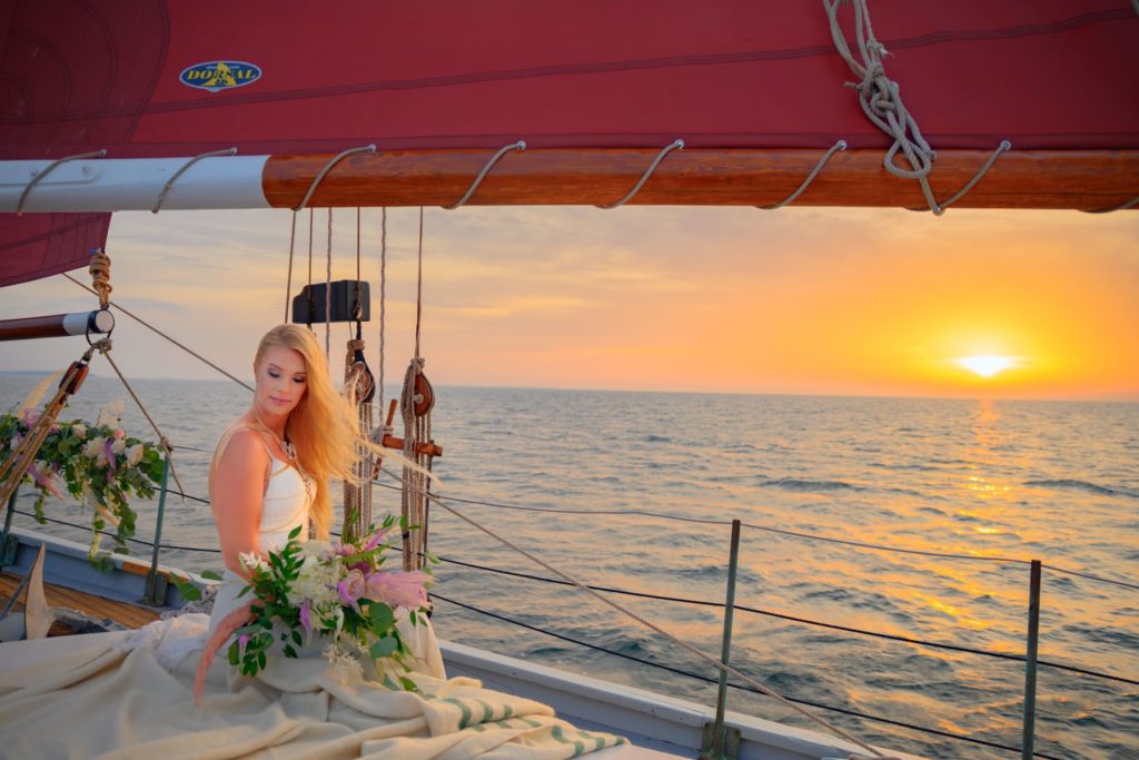 A bride sits under the sail of a sailboat for her Wisconsin sailboat elopement in Door County, WI at sunset