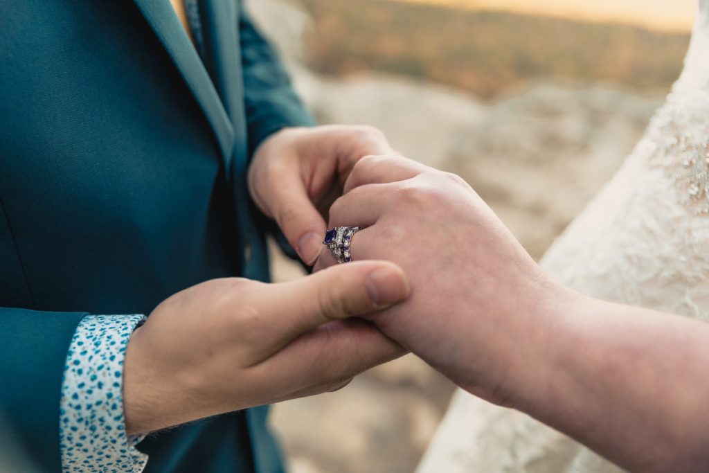 After saying their vows, the couple exchanges rings. They chose purple amethyst and diamond for her wedding band and purple amethyst and wood for his wedding band.