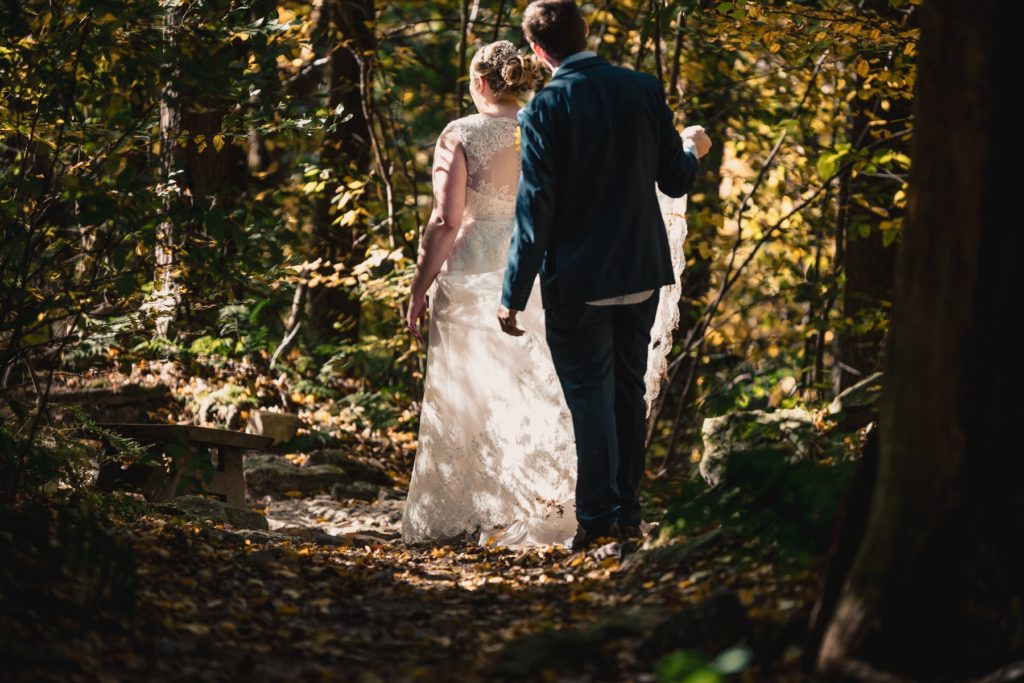 Hiking through the mountains of Pennsylvania, the groom helps his bride with the train of her white lace wedding dress.