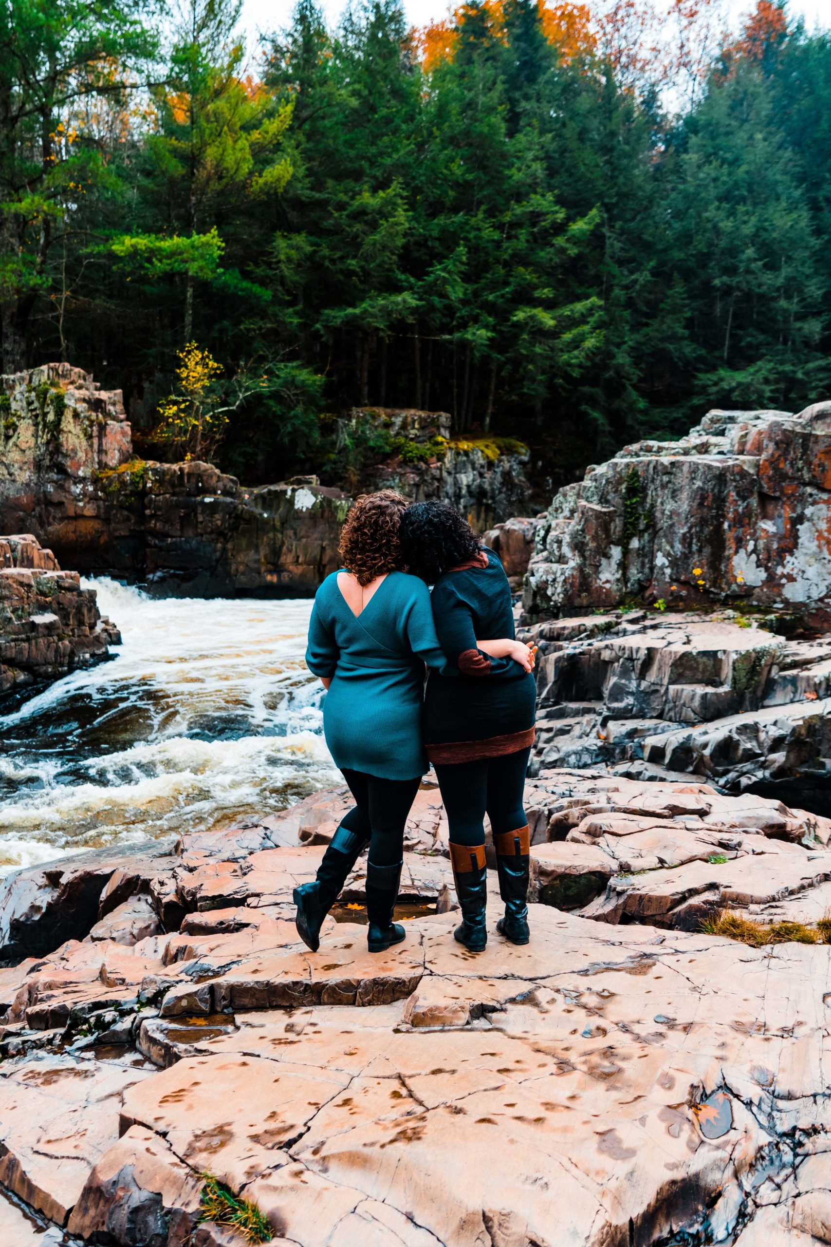 A couple lovingly embraces on a rock outcropping in the middle of a river, as they pose for their engagement pictures.