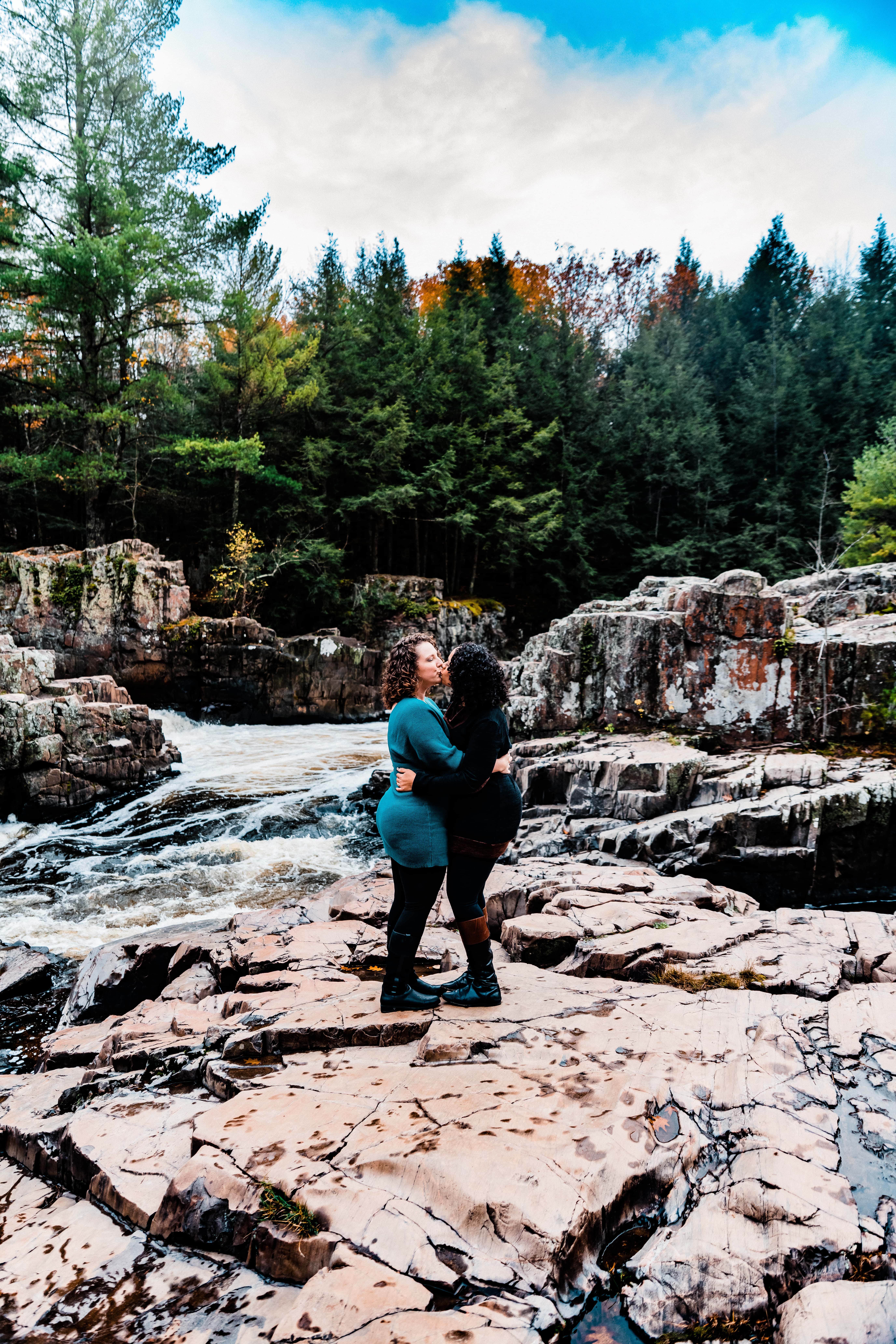 Kissing on a rock formation in the middle of the river, a couple poses for the camera during their Wisconsin engagement pictures