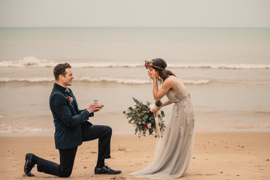 A man on one knee asks his girlfriend to marry him as the waves roll in along the beach of Lake Michigan