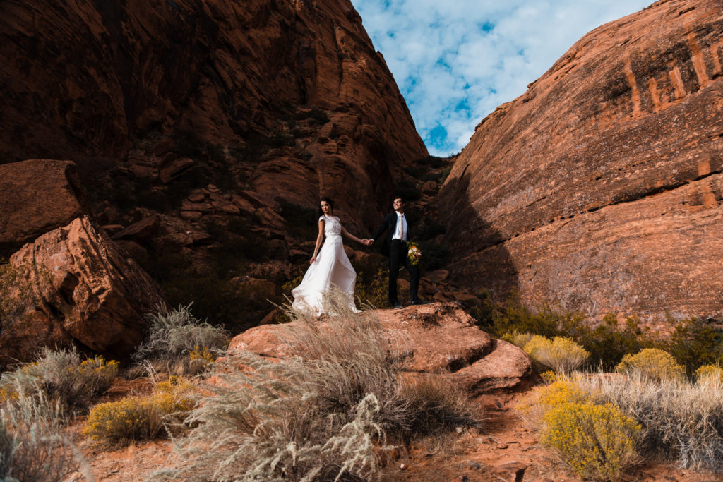 An eloping couple stands a top a huge rock as they pose for their wedding portraits in southern Utah