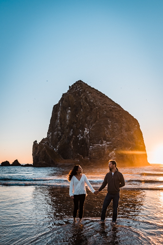 Walking towards the camera, this engaged couple holds hands near during sunset near Haystack Rock on Cannon Beach on the Oregon Coast