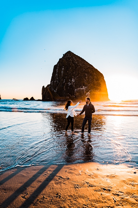 Holding hands at sunset, an engaged couple walks Cannon Beach during their Oregon engagement session