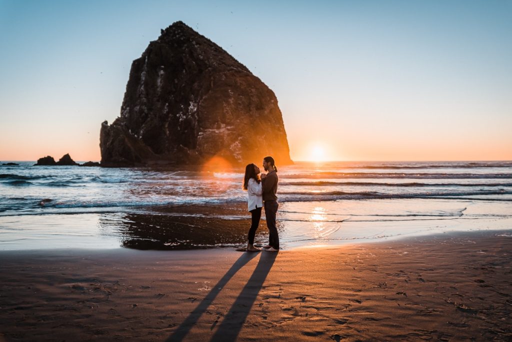 Holding each other, this engaged couple poses for their engagement pictures near Haystack Rock on Cannon Beach in Oregon