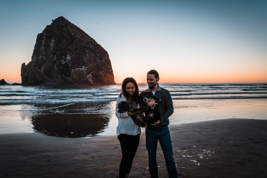 Holding their dogs, this engaged couples smiles during sunset during their engagement photos on Cannon Beach on the Oregon Coast