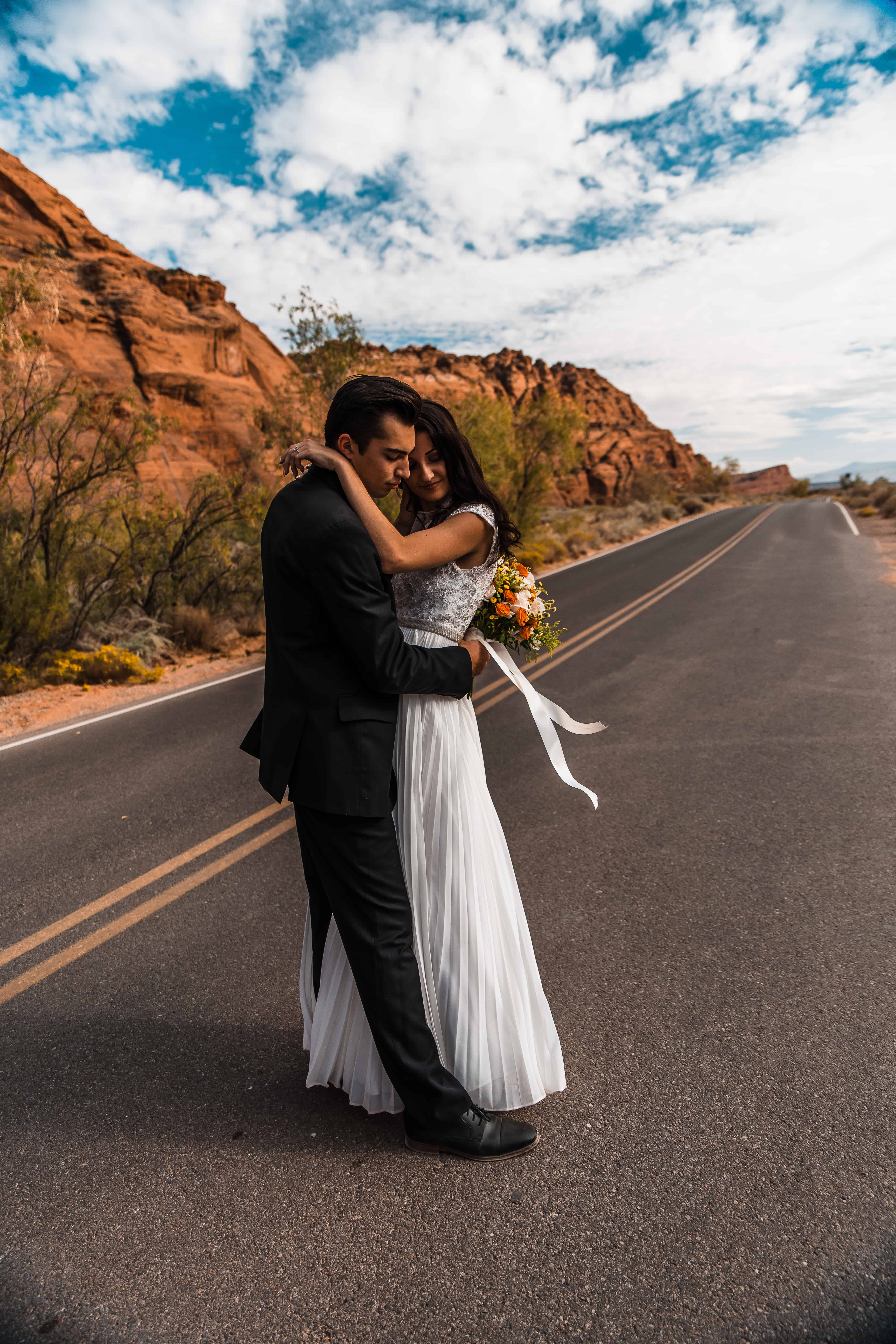 A couple wearing wedding attire embraces after their first look in the road