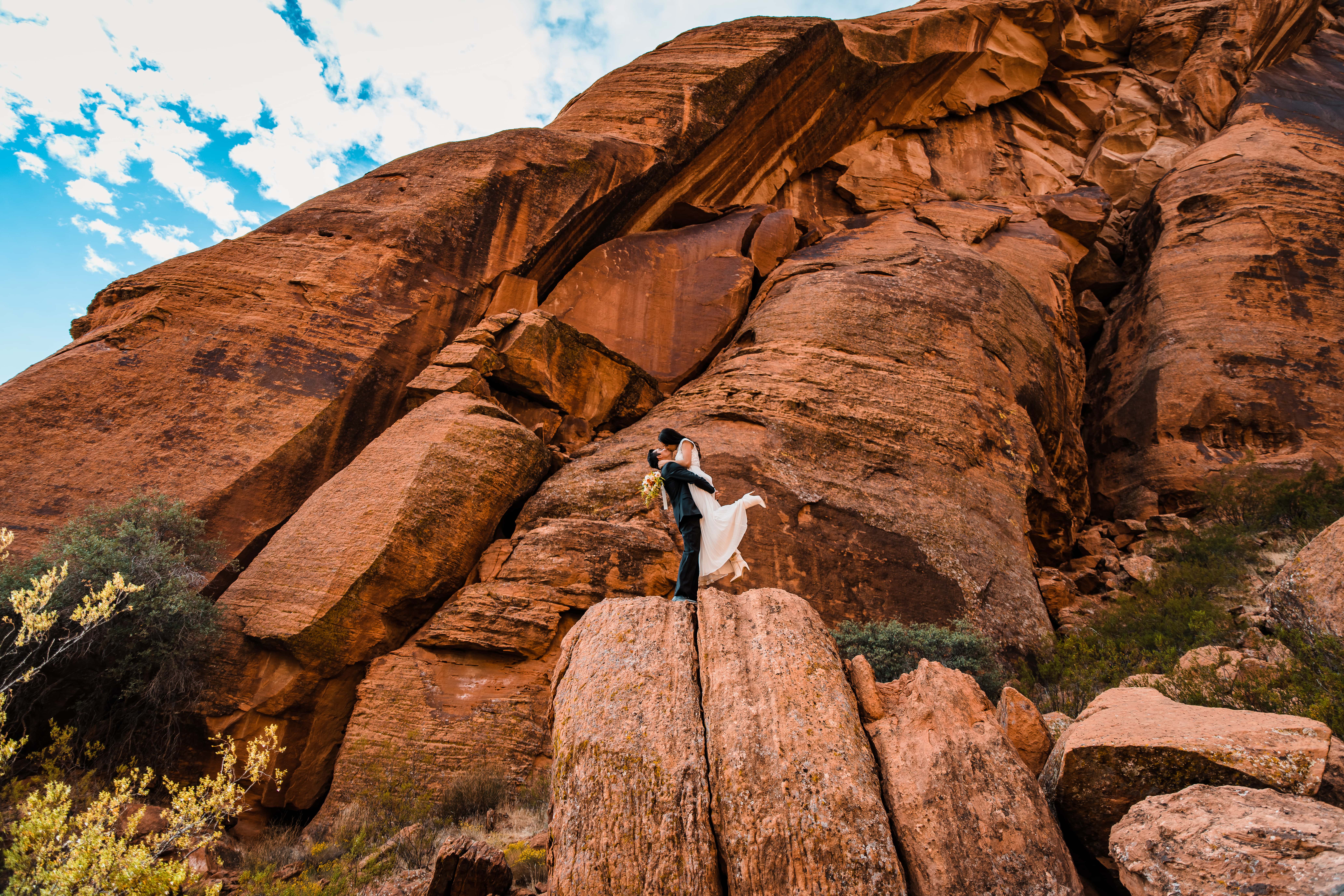 A couple in wedding attire stands atop a large rock formation as they elope in utah.