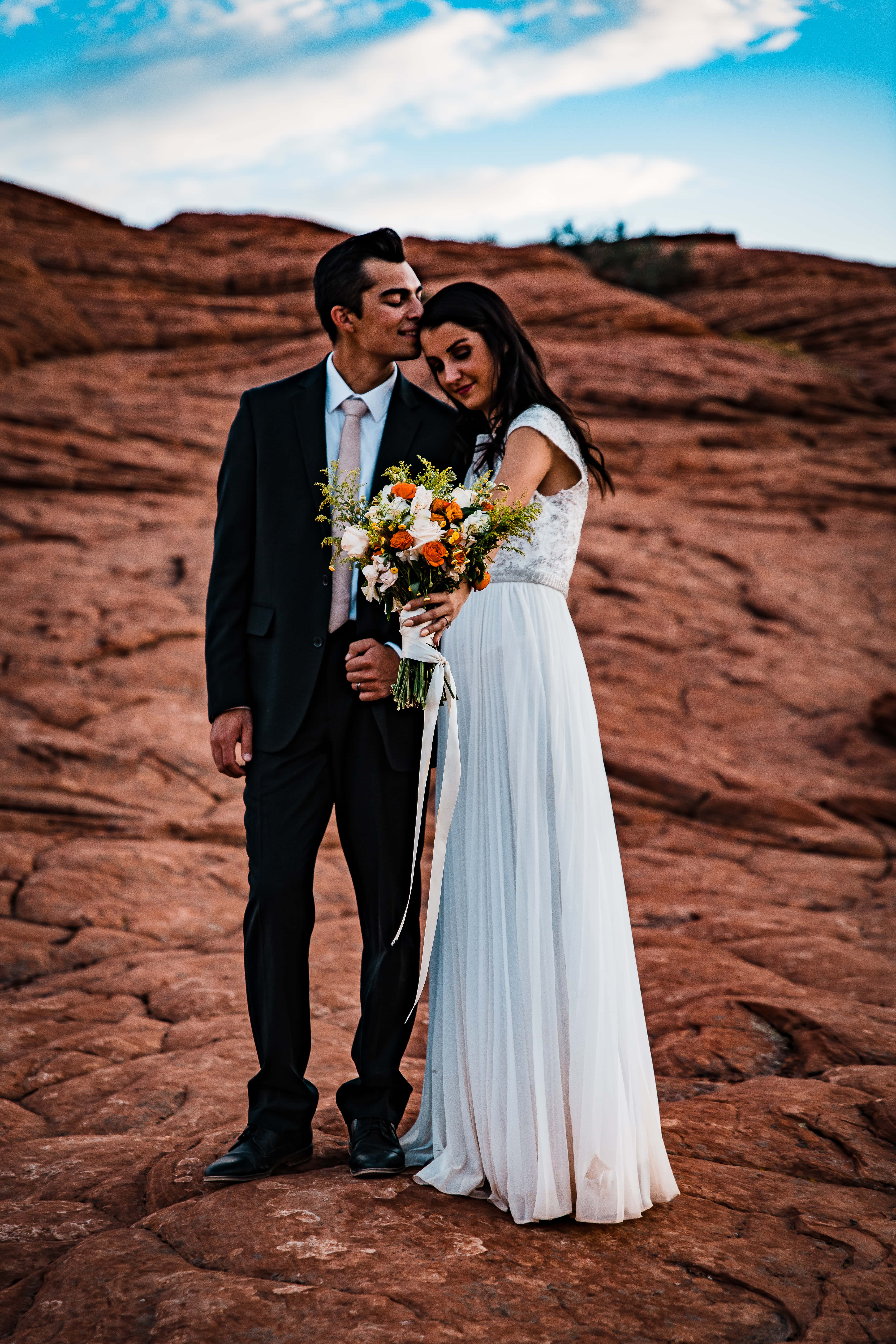 A newly eloped couple embraces with a wedding bouquet in southern Utah's red rocks.